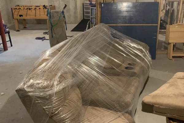 Couch wrapped in plastic in the basement of a home being moved.